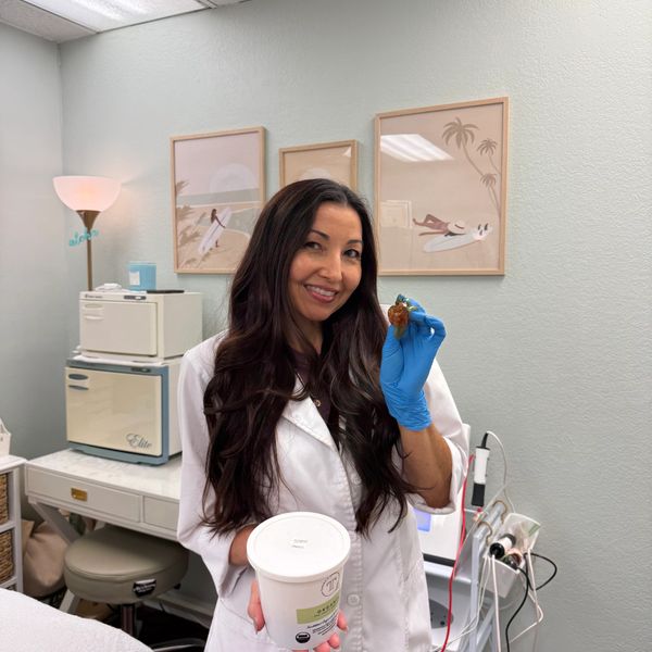 Smiling woman in lab coat holding a sample and container in a clinical setting.