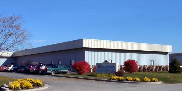 Industrial building with parked cars and autumn landscaping under a clear blue sky.