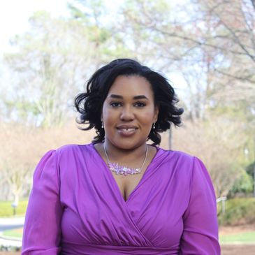 Woman in a purple dress smiling outdoors.