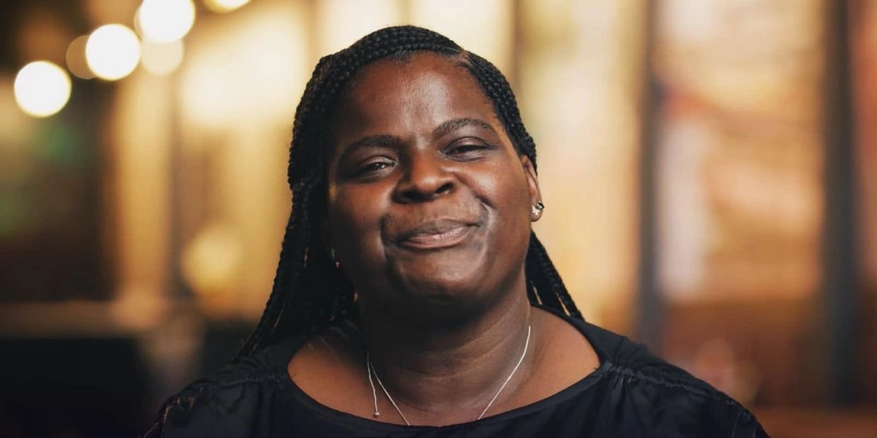 Smiling woman with braided hair and a dark top.