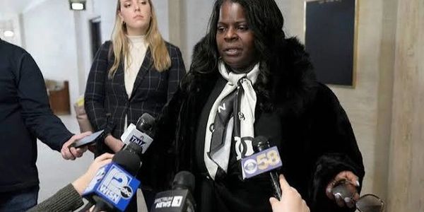Woman speaking to reporters with microphones.