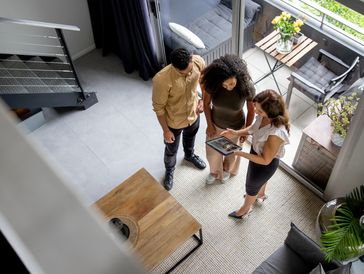 Three people looking at a tablet in a modern living room.