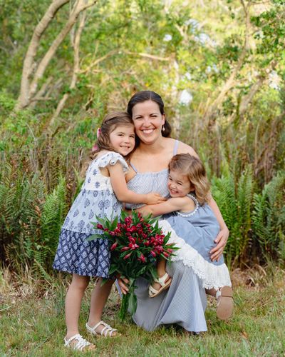 A happy mother with her two daughters outdoors, holding a bouquet of flowers.
