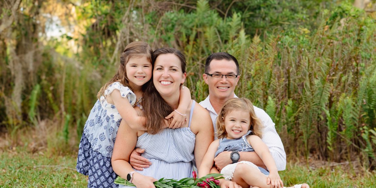 A happy family of four sitting on a blanket outdoors with flowers.