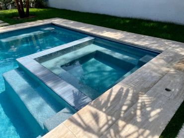 Modern pool with a built-in hot tub and stone surroundings.