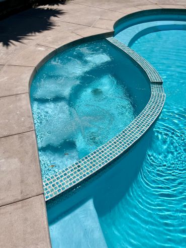 Curved jacuzzi with bubbling water next to a swimming pool.
