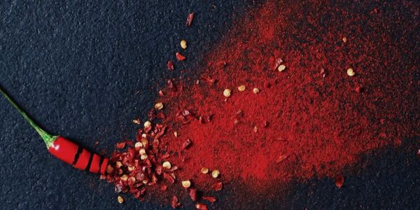 Red chili pepper and crushed chili flakes on a dark surface.