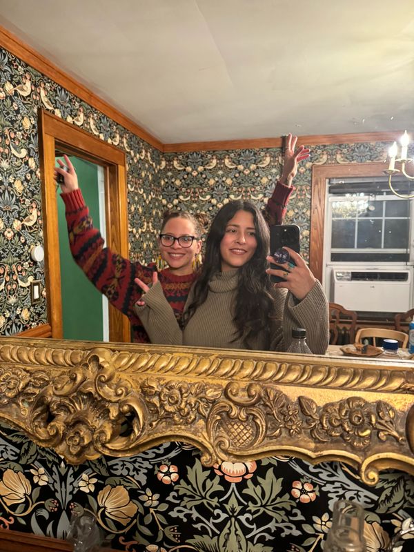 Two friends pose happily for a mirror selfie in a vintage-style room.