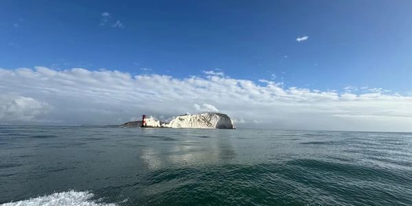 Ocean view with a rocky island and red-white striped lighthouse under blue sky.