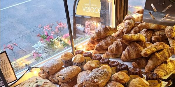 Bakery display with croissants, pain au chocolat, cinnamon rolls, and pastries by a window 