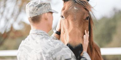 A soldier gently pets a horse's face in an outdoor setting.
