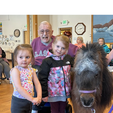Two young girls with an elderly man and a miniature horse indoors.