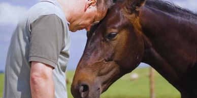Man and horse share a gentle moment, touching foreheads.