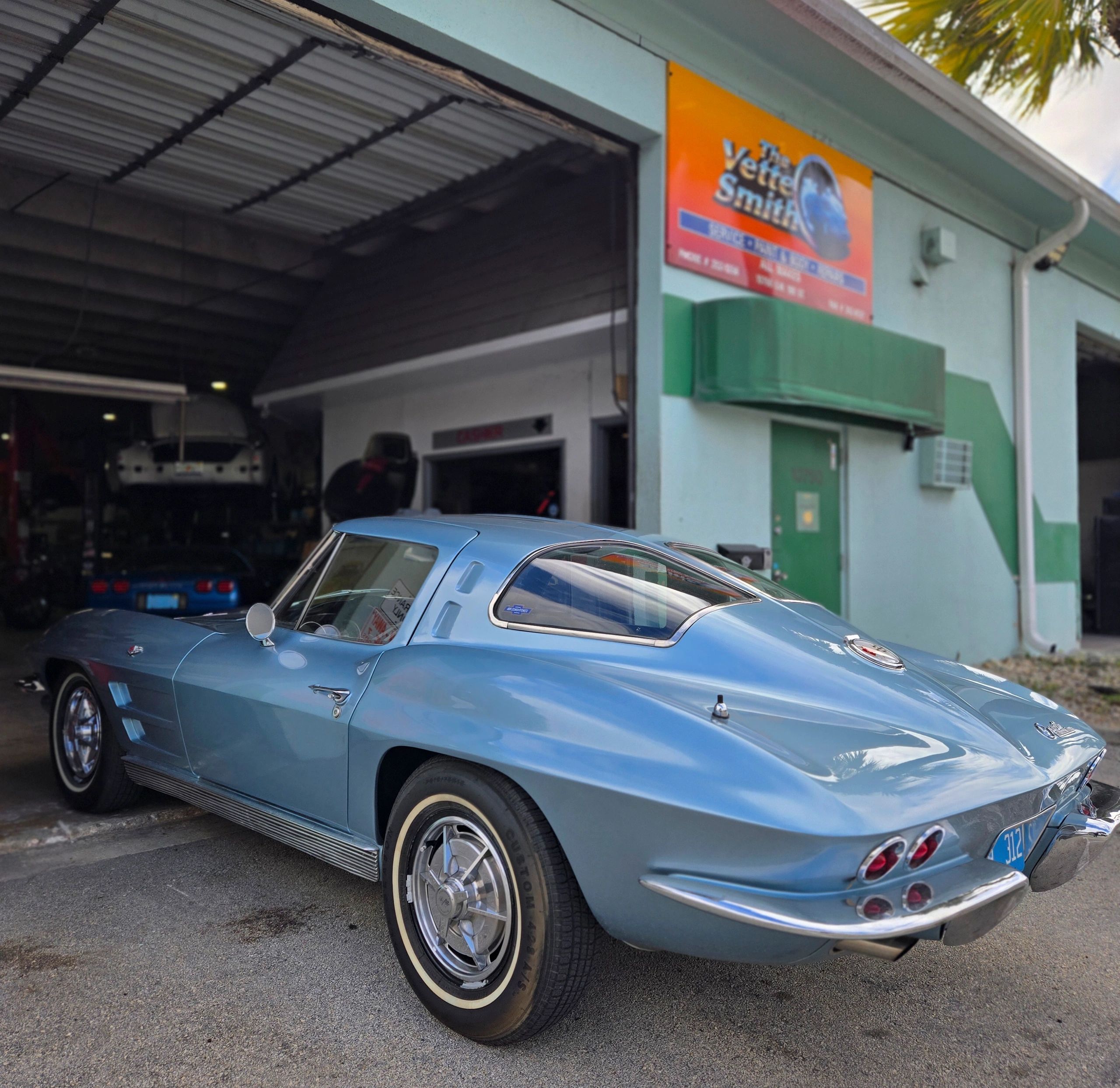 Classic blue Corvette parked outside an auto repair shop.