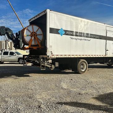 A logistics truck with a large spool being loaded by a red crane.