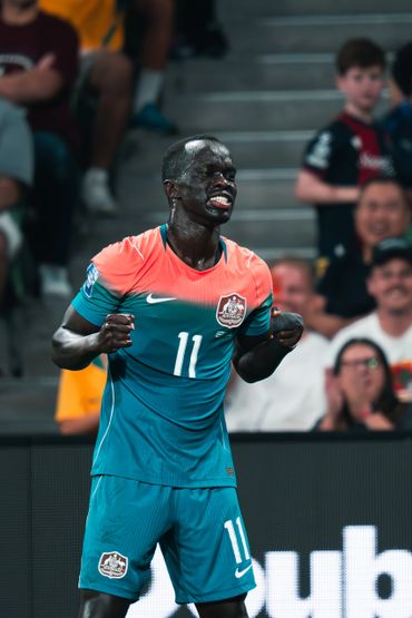 Soccer player in teal and orange jersey celebrating with clenched fists.