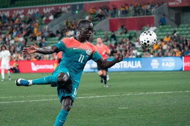 Soccer player in teal uniform skillfully kicks the ball mid-game.