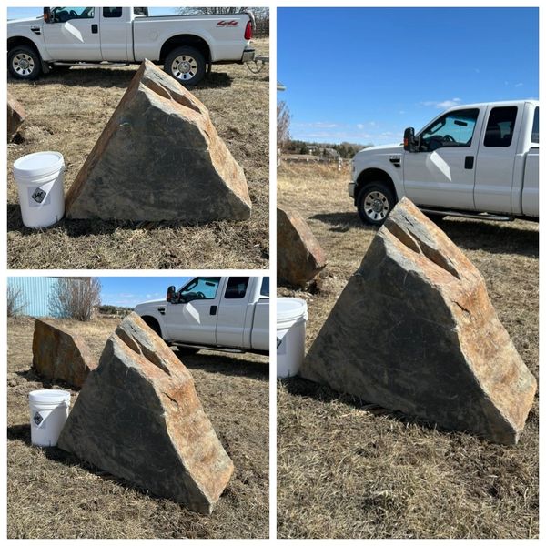 Large triangular boulder next to a white bucket and truck.