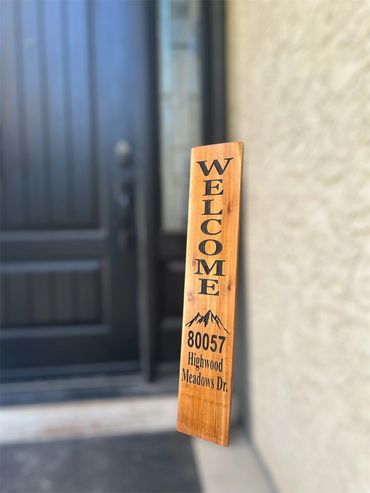 Wooden welcome sign with address in front of a black door.