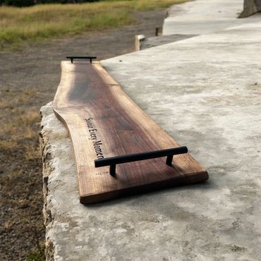 Wooden serving tray with handles on a stone surface outdoors.