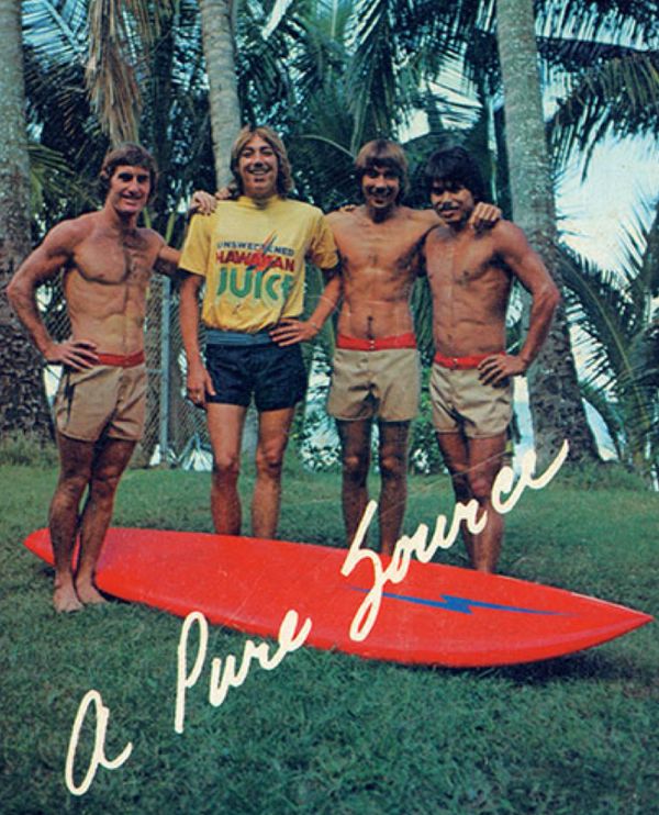 Four men with a red surfboard and tropical background.