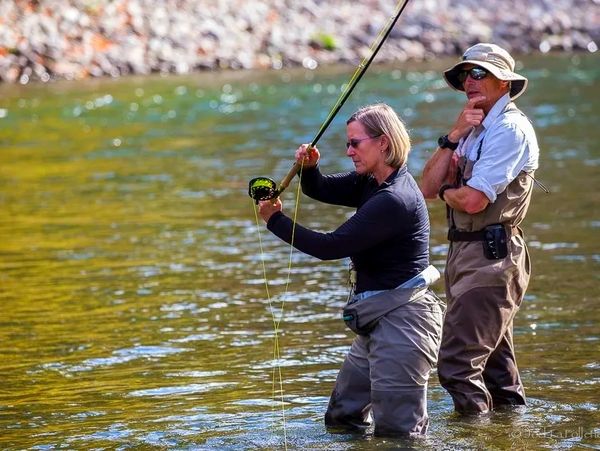 Two people fly fishing together in a river, both wearing fishing gear.