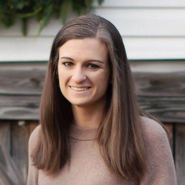 A smiling woman with long brown hair in a beige sweater.
