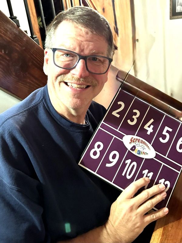 Smiling man holding a scoreboard with numbers.