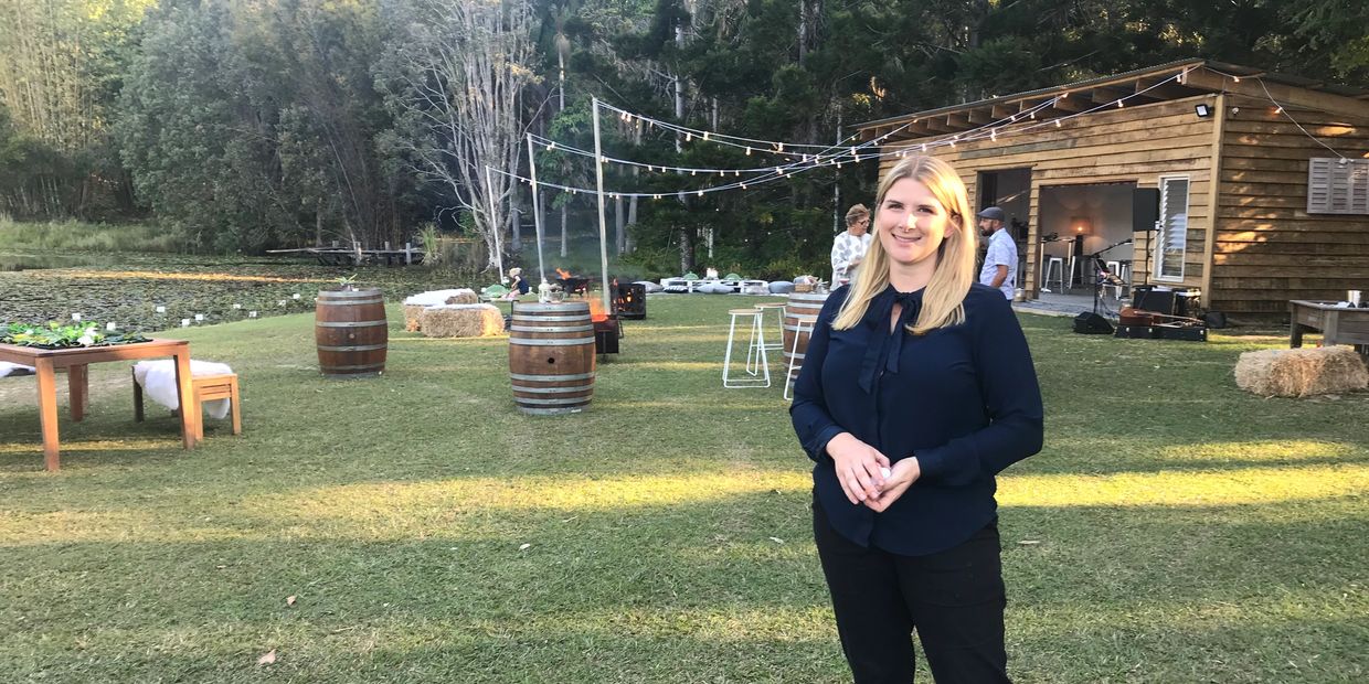 Woman standing in a grassy outdoor space with a wooden cabin and barrels.