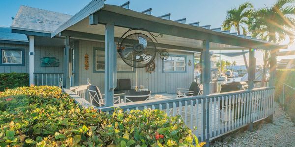 Waterfront home with a covered deck, seating, fan, lush greenery, & canal views in the Florida Keys.
