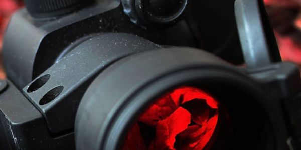 Close-up of a rifle scope with a red illuminated reticle.