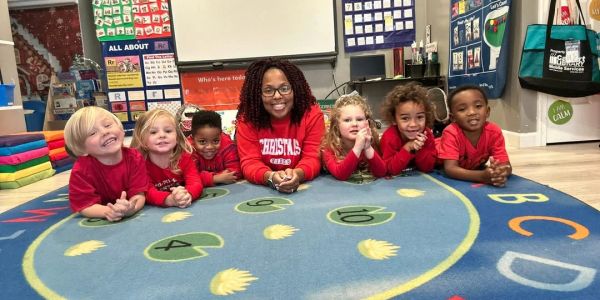 Teacher with six young children lying on a colorful classroom rug.