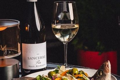 A glass of white wine with a bottle and a gourmet fish dish.