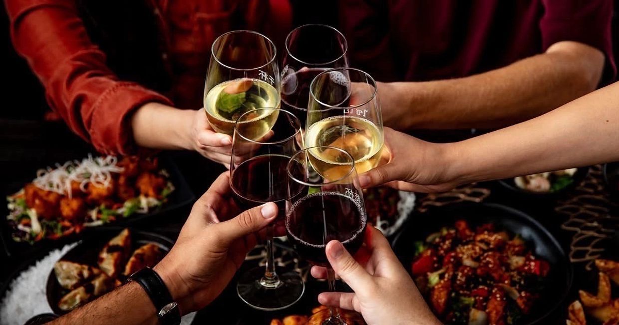 Friends clinking wine glasses over a table full of delicious food.