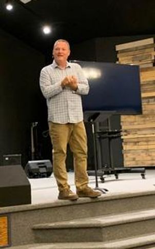 Pastor standing on a stage in front of a monitor, clapping and smiling