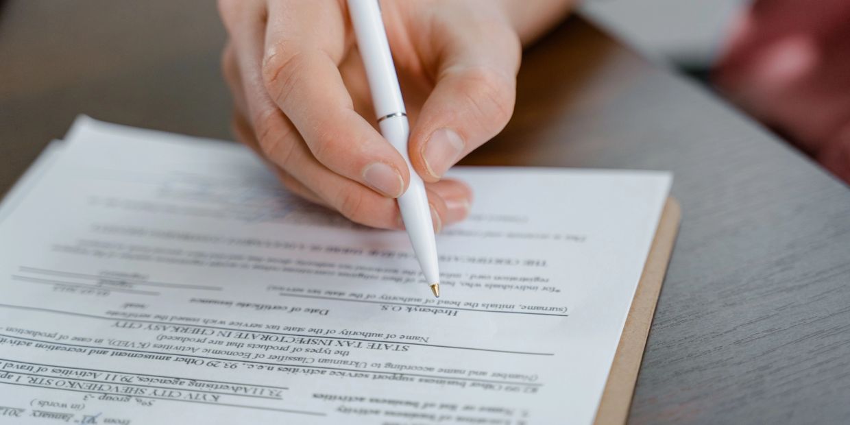 Hand signing a document with a white pen.