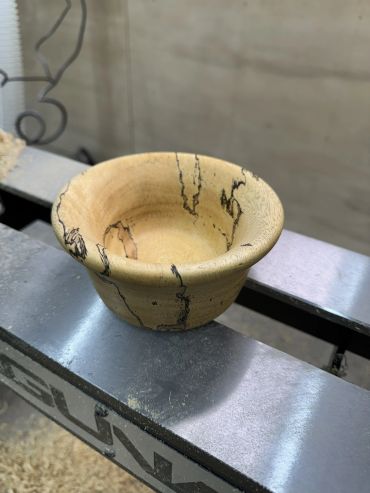 Handcrafted wooden bowl with natural black streaks on a metal surface.