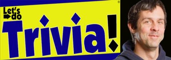 A man standing next to a bright sign that says 'Let's do Trivia!'