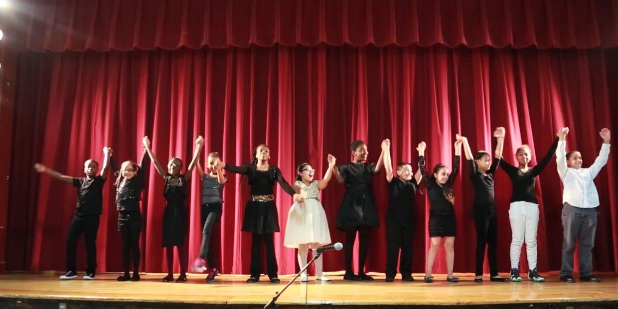 Children holding hands on stage after a performance.