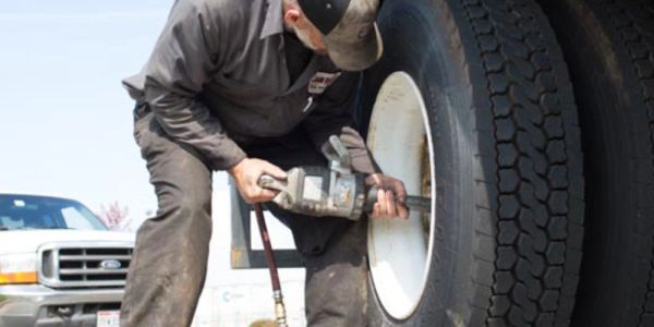 Mechanic using power tool on large truck tire.