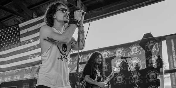 Rock band performing on stage with American flag backdrop.