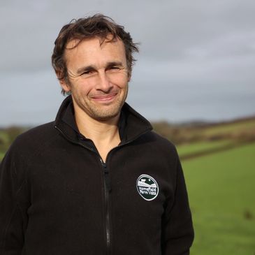 Man in black jacket smiling outdoors.