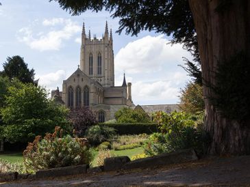 A historic church tower rises above a lush garden under a blue sky.