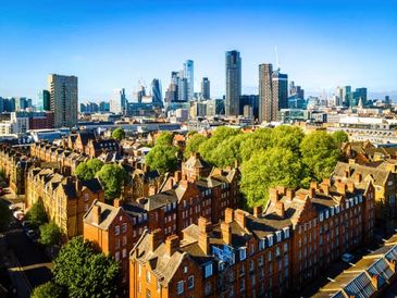 A cityscape with tall modern buildings and historic red brick houses under a clear blue sky.