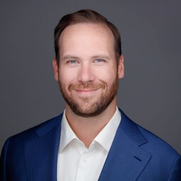 Professional headshot of a smiling man in a blue suit and white shirt.