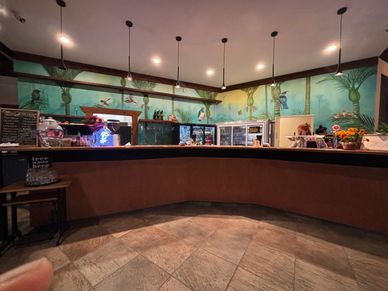 Cozy cafe counter with tropical bird mural and warm lighting.
