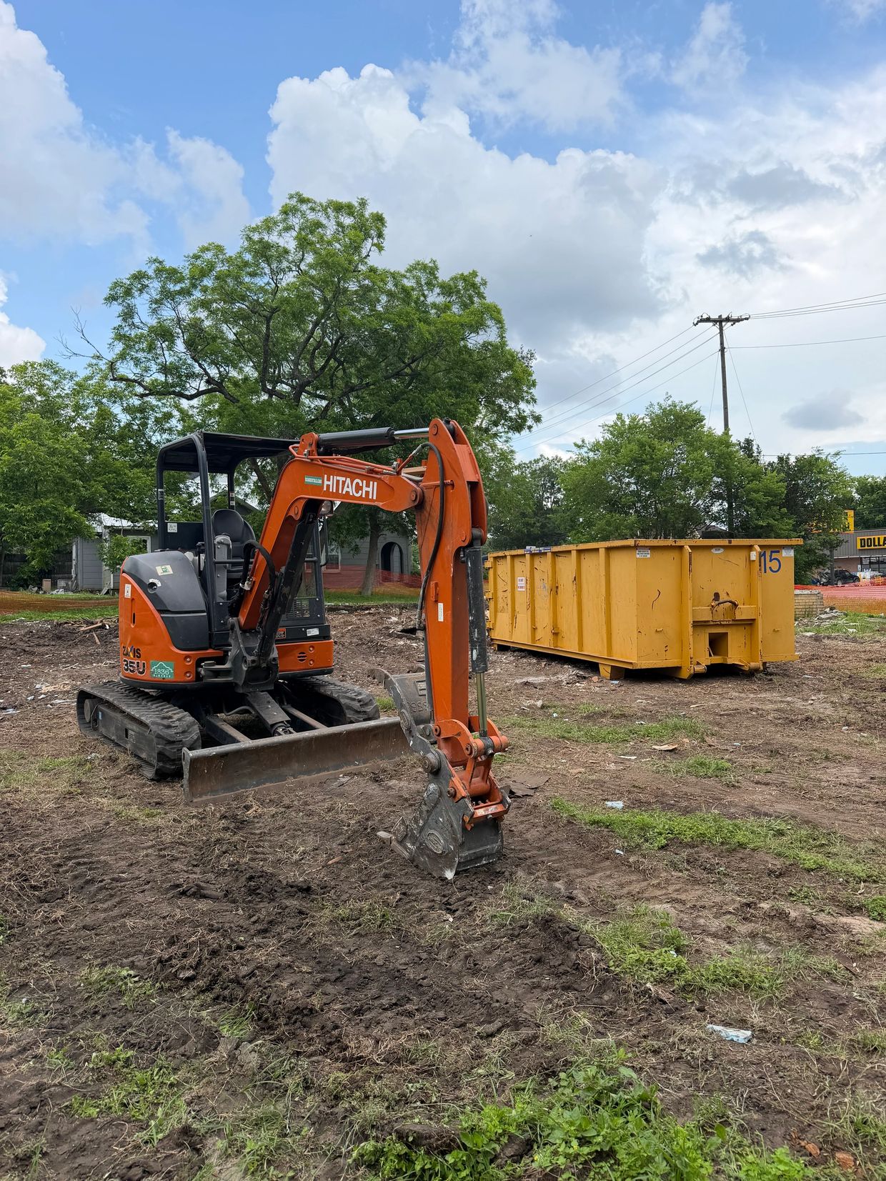 Orange Hitachi excavator at a construction site with a yellow dumpster.