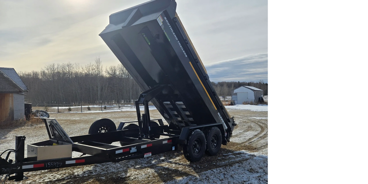 Black Southland dump trailer raised on snowy ground near buildings.
