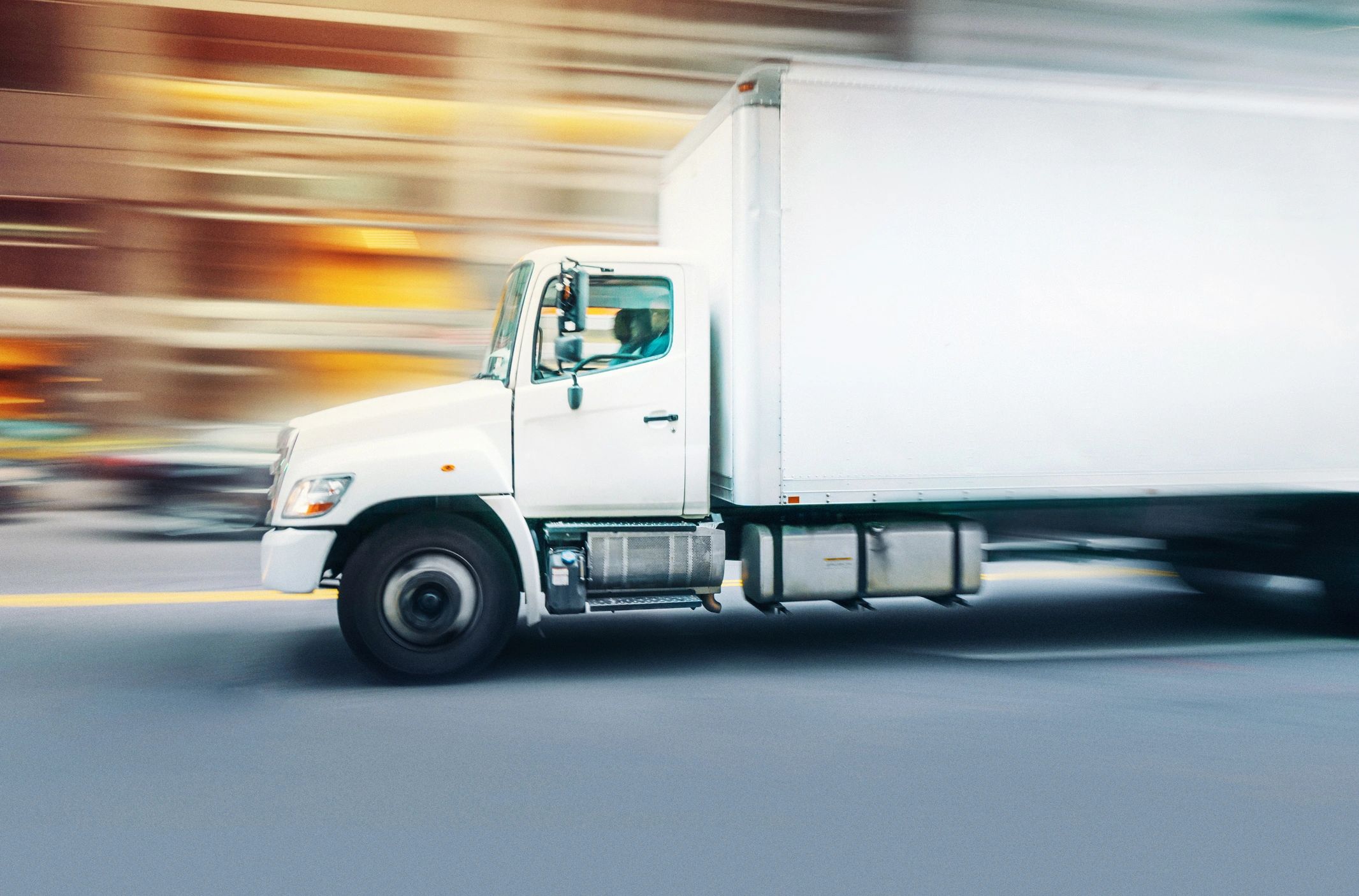 White delivery truck driving fast on city street.
