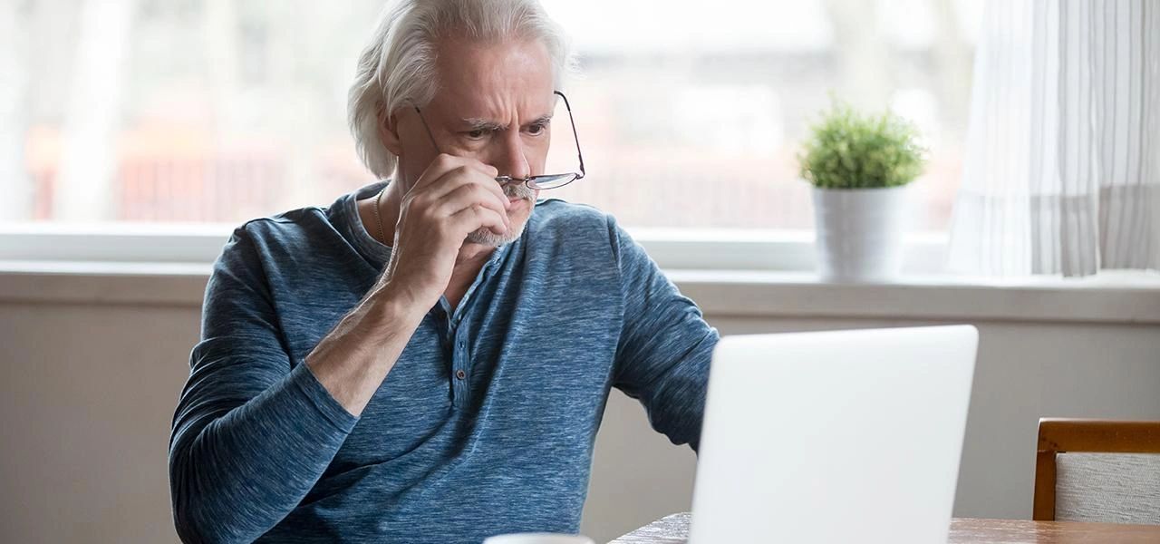 An elderly man adjusting his glasses while looking at a laptop screen.